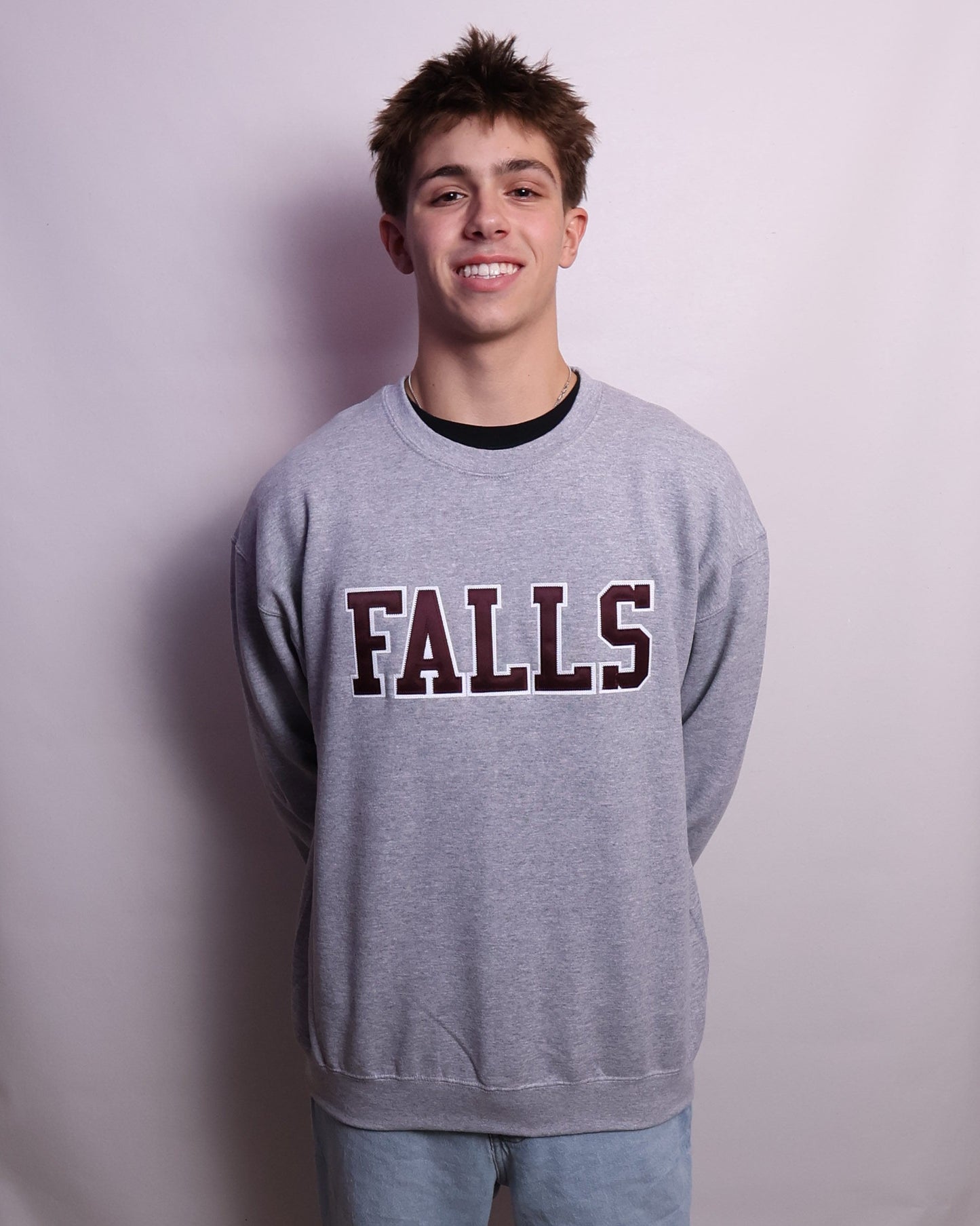 Person wearing a sweatshirt with 'FALLS' printed on it, standing on a white sheet in a room.