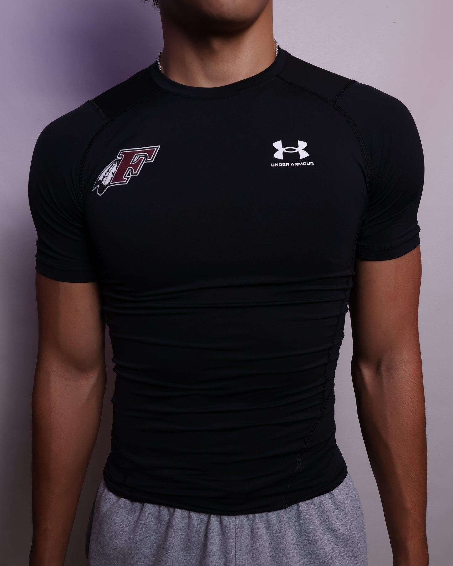 Person wearing a black Under Armour shirt with a logo on a plain background