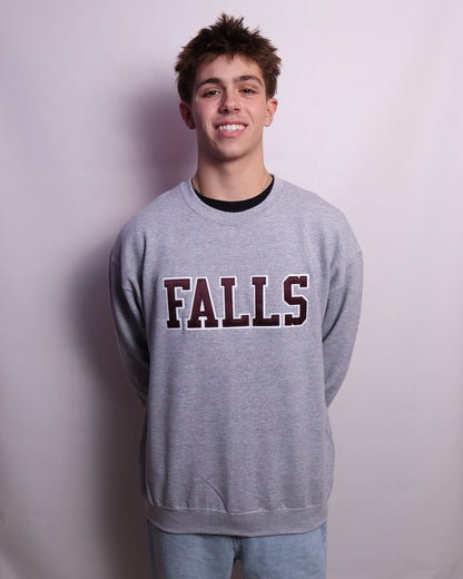 Person wearing a sweatshirt with 'FALLS' printed on it, standing on a white sheet in a room.